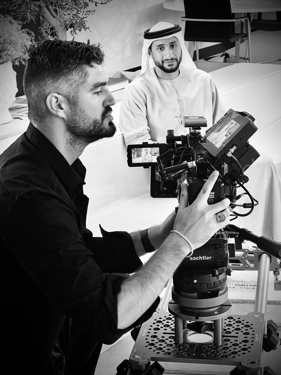 Black and white photo of Rian framing an interview with an Emirati subject
